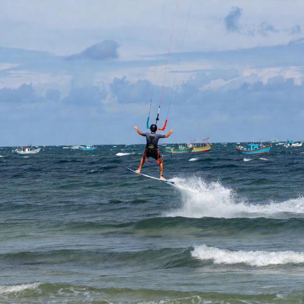 Kitesurfer mid-jump over waves with fishing boats.