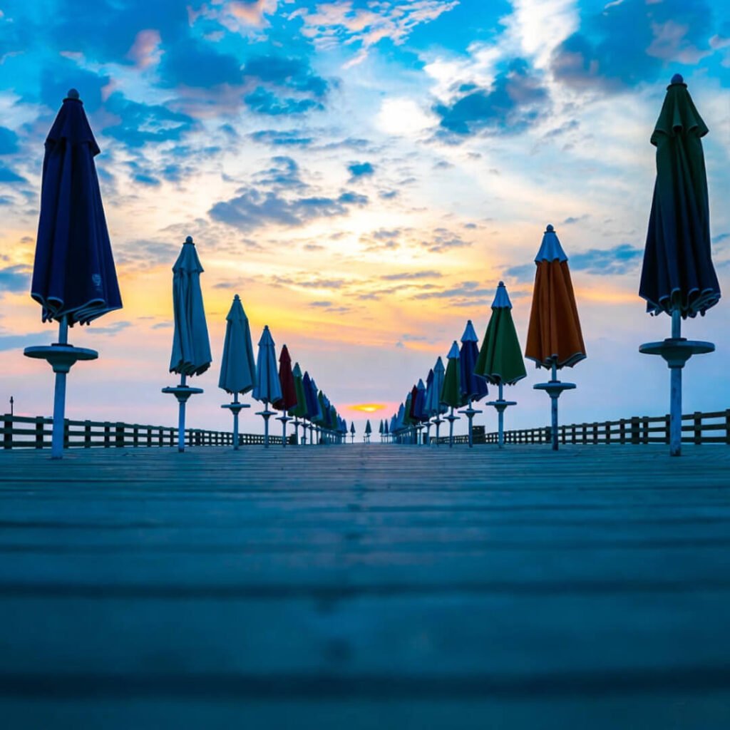 Empty boardwalk with closed umbrellas at moody sunset.