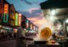 Travel to Malaysia: The Ultimate Adventure for Foodies and Nature Lovers street scene in Kuala Lumpur at dusk. Neon hawker stall signs glow against humid night air.