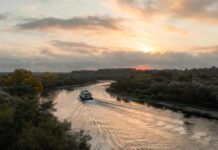 Calm river scene at sunset, ferry passing, muted blues and golds